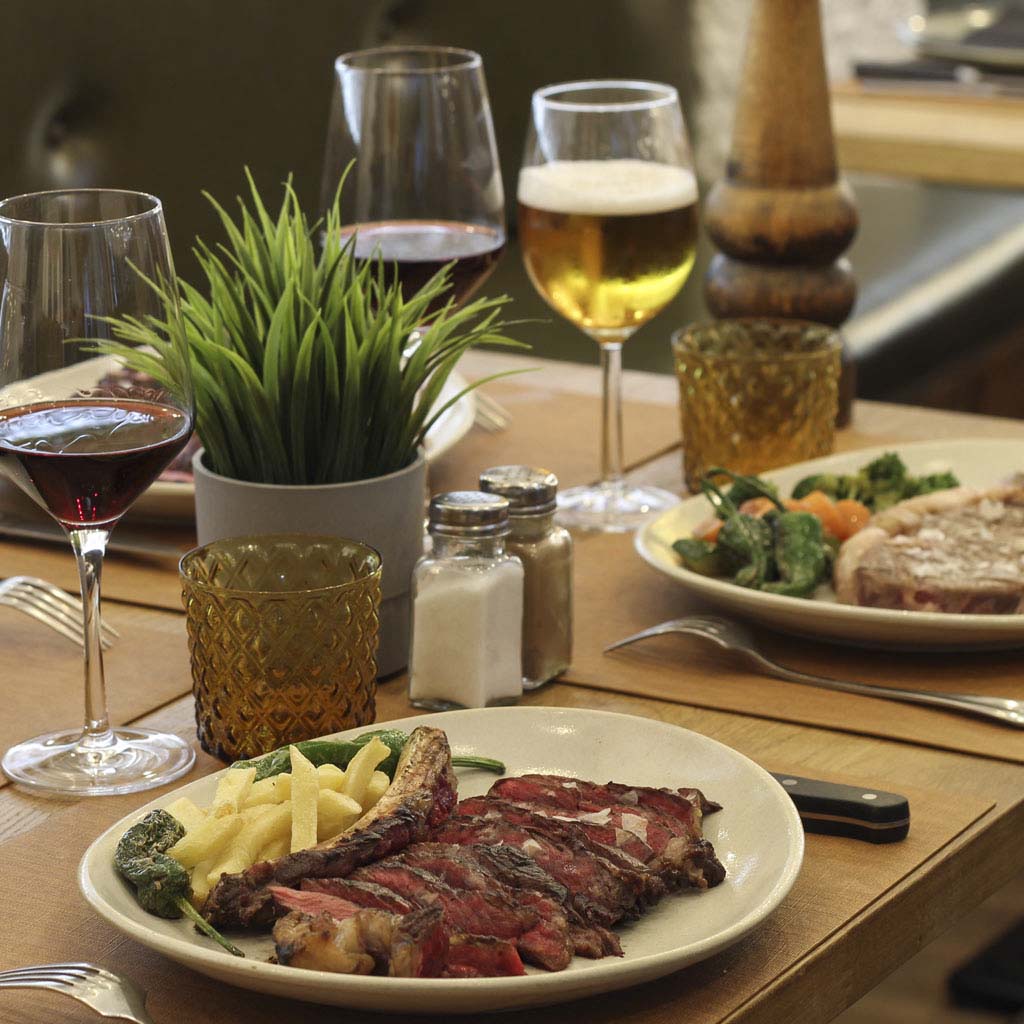 Mesa con carne de vaca vieja a la brasa, patatas fritas y copas de vino en The Beefeater